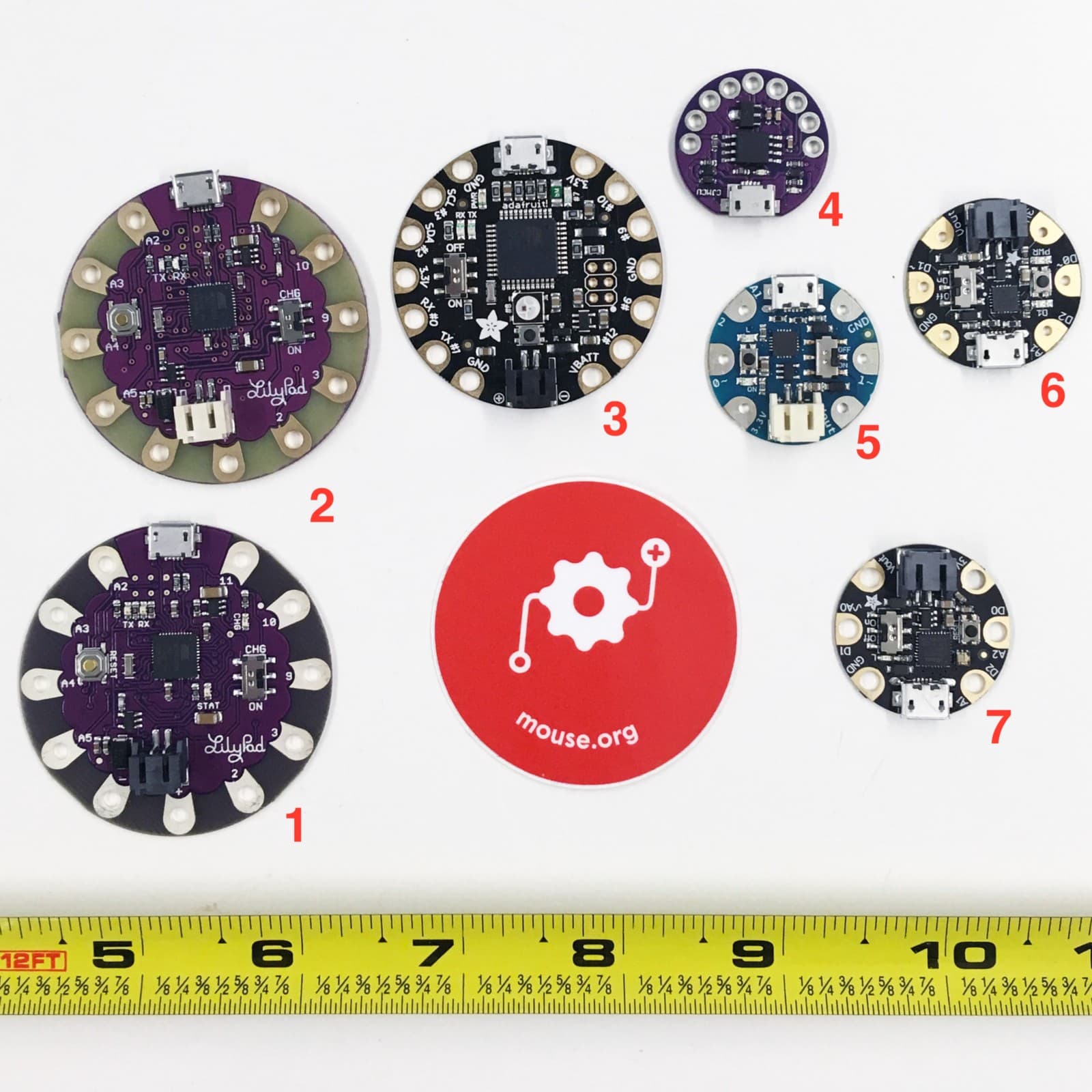 A picture of 7 different sewable microcontrollers and a Mouse sticker